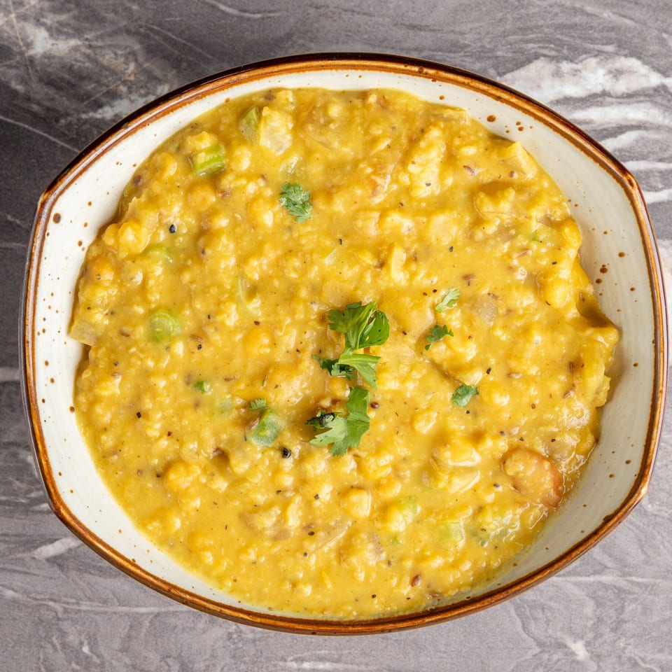 A bowl of yellow Indian dal, garnished with fresh cilantro, on a gray marble surface.