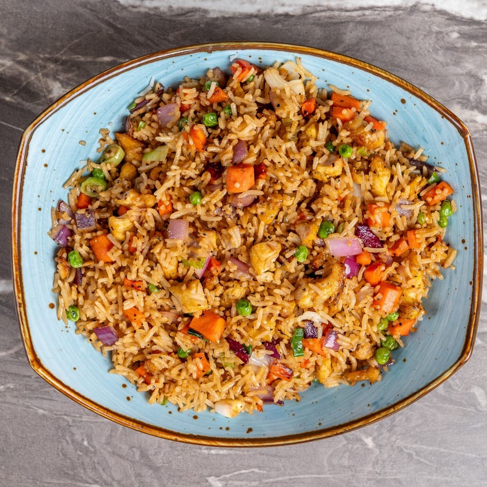 A blue bowl filled with Indian-style fried rice, chicken, carrots, peas, and red onions.