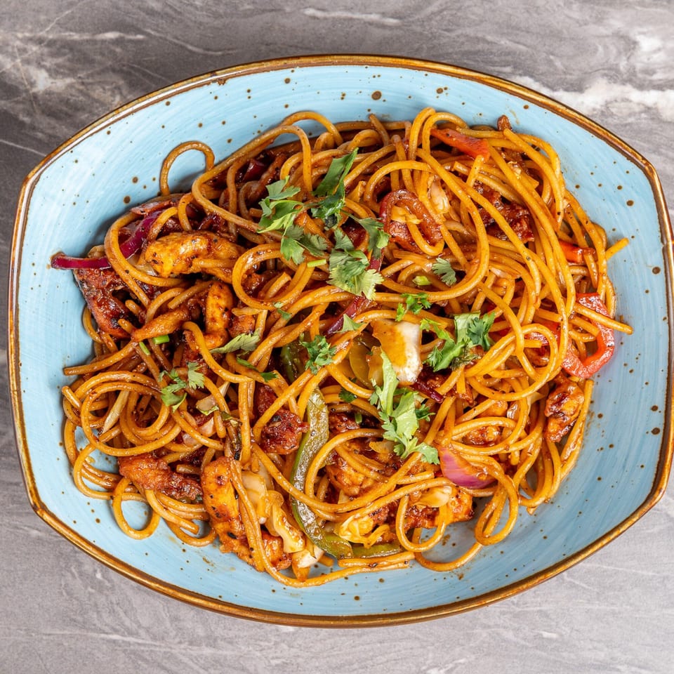 A blue bowl filled with Indian-style noodles, chicken, red onions, and green peppers, garnished with cilantro.