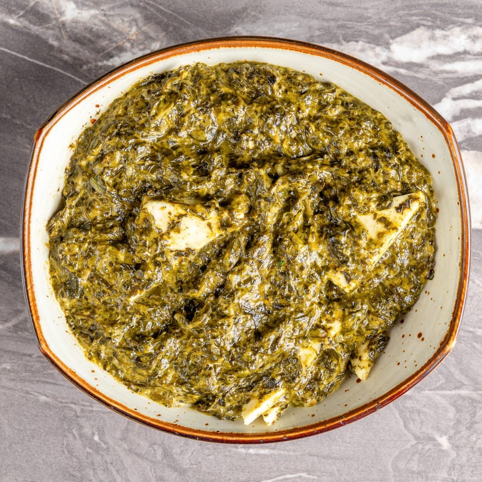 Overhead view of a bowl of vibrant green Saag Paneer with visible cubes of cheese.
