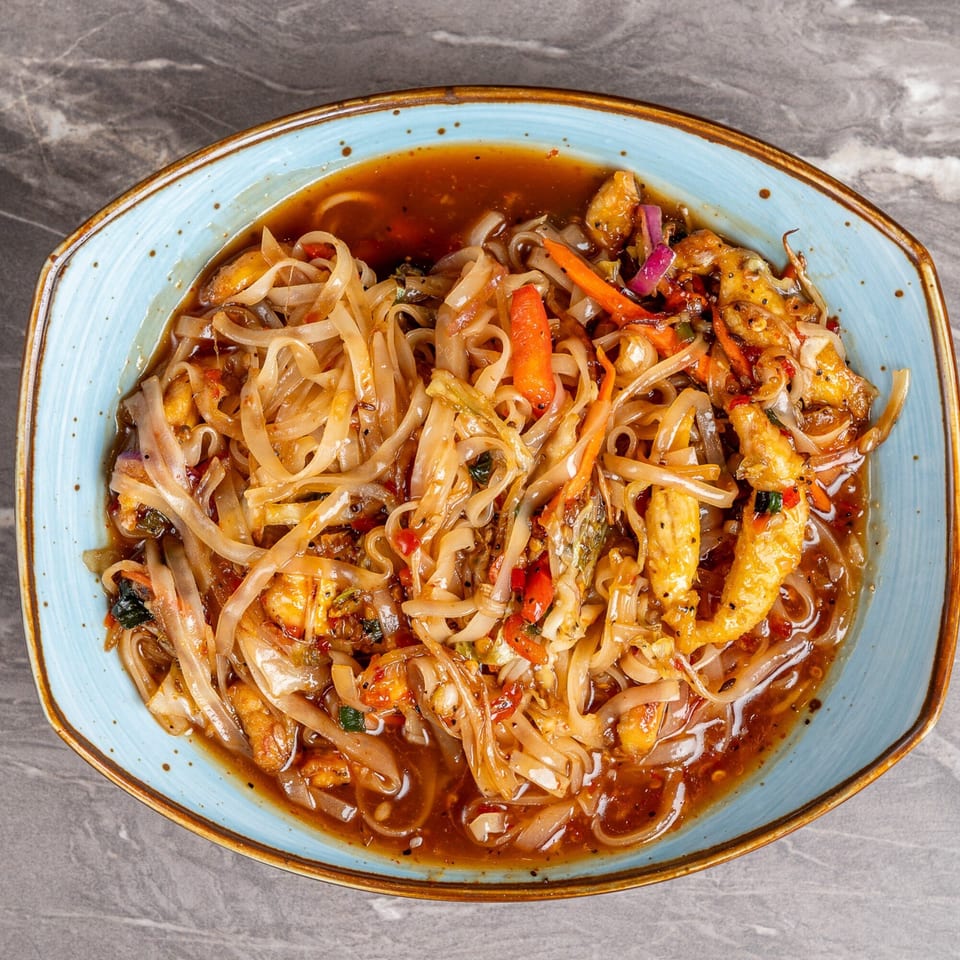 A blue bowl of Indian noodles with chicken, carrots, and onions in a rich sauce.