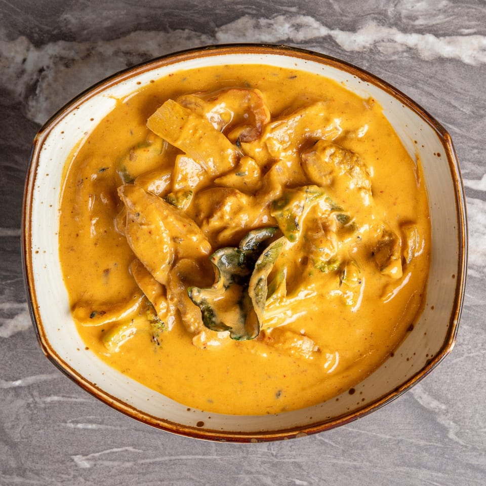 Overhead view of a bowl of Indian curry with chicken and vegetables in a rich orange sauce.