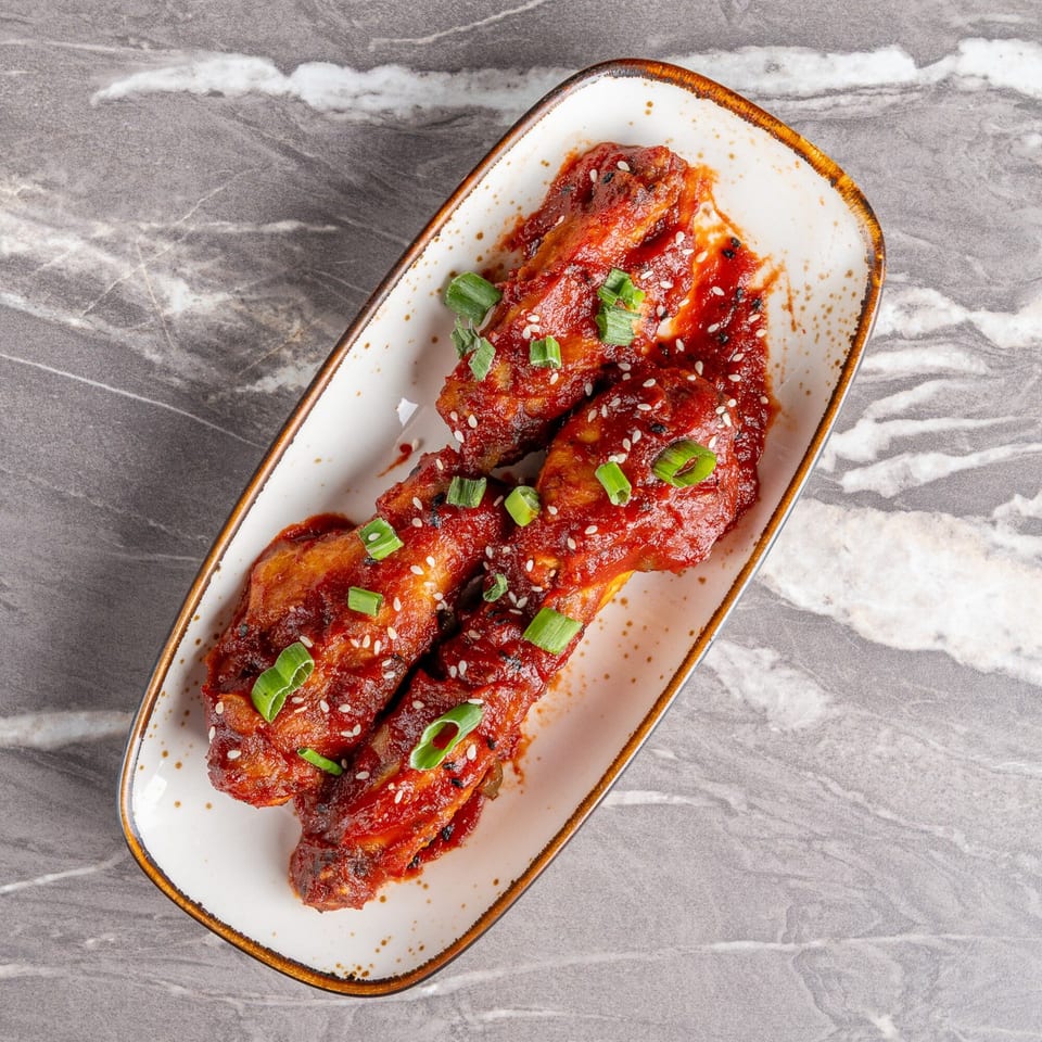 Spicy chicken wings, garnished with sesame seeds and green onions, on a white rectangular plate.