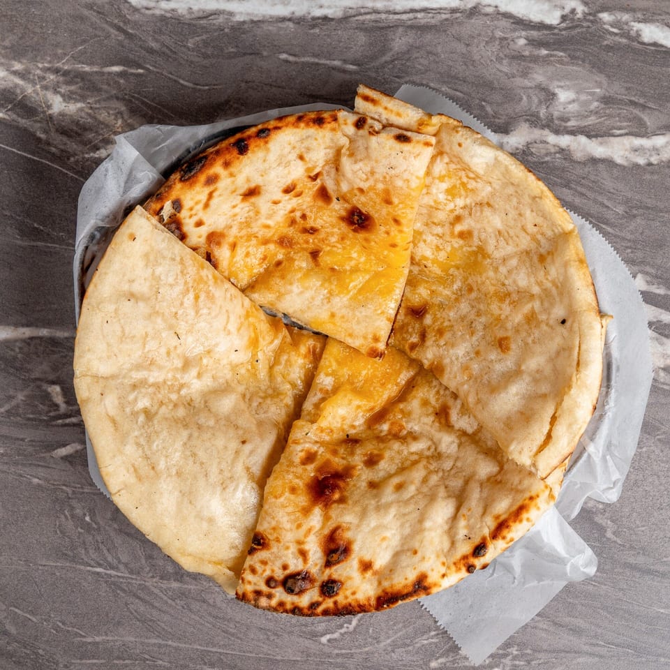 Golden-brown Indian naan bread, cut into wedges and served on white paper in a basket.