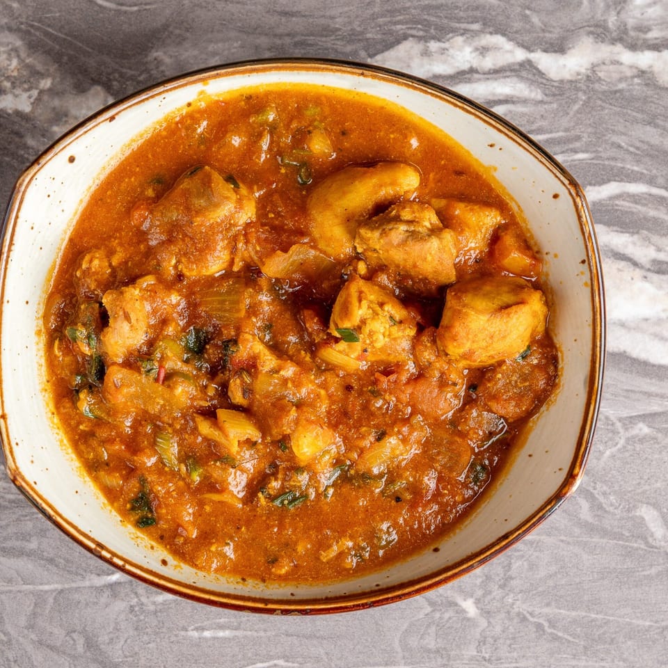 Close-up of a bowl of Indian chicken curry with potatoes and vegetables in a rich orange sauce.